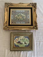 Top-down view of two framed Persian style paintings placed on white fabric surface, showcasing detailed ornate framing and intricate oil painting details.