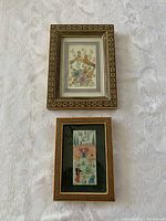 Two small framed prints laid flat on a white floral textured surface, illustrating the full lot contents.