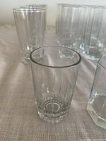 Photo showing several types of clear water glasses, some tall and cylindrical, others shorter with ridges, placed on a cloth surface.