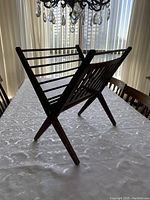 Wooden foldable magazine rack shown from an angled side view on table with curtains background