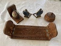Overall view of five decorative wooden and metal pieces on a white lace tablecloth, showing the arrangement of carved wooden items and book ends.
