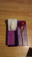 Single 24K gold plated red rose with gold-plated stem presented in a purple box with a white ceramic vase set in a foam insert.