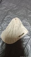 White knitted Billabong beanie laid flat on a dark textured surface.
