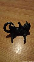 Top view of black cast iron cat figurine lying on wooden surface, showing raised legs and curled tail.