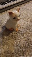 Front view of the white ceramic cat figurine with painted details sitting on a carpeted floor.