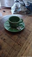 Green ceramic teacup and saucer with rabbit and carrot design on wooden surface.