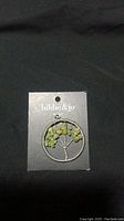 Front view of Hildie & Jo costume jewelry pendant on black background, showing tree design with green bead foliage attached on the original display card.