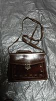 Brown real leather box bag laying flat on a textured surface, showing front, strap and clasp.