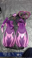 Full set of purple and pink woman's snorkeling gear including fins, mask, snorkel, and fishnet carry pouch laid out on a surface.