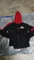 Photo of a black and red boys windbreaker hoodie laid flat, showing front side with full zip and hood.