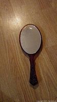 Front view of vintage antique hand mirror showing oval mirror and decorative handle on wood floor.