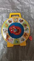 Front view of vintage yellow circular kids toy with animal pictures and red lever.