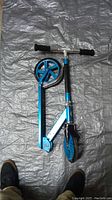 Folded Razor scooter showing blue frame, wheels, and handlebars with foam grips on a tarp surface.