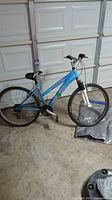 Blue Schwinn Ranger girls mountain bike leaning in garage. Flat rear tire and missing left handlebar grip visible.