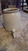 White ceramic water dispenser with attached white spigot, shown on carpet