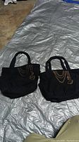 Photo of two black women's cloth purses with chain and charm designs on a silver tarp background.