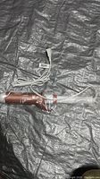 Photo of the curling iron showing rose gold barrel and white handle with attached white power cord, wrapped in clear plastic packaging.