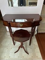Rectangular wooden side table with drawer showing scalloped edges and turned legs, placed on tiled floor against wall.