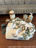 Photo displaying several bathroom items including ceramic containers with lids, soap dispenser, toothbrush holder, small basket, and folded fabric shower curtain.