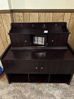 Front view of the two-piece wooden bench and storage set against a paneled wall and carpeted floor.
