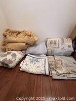 Blankets folded and stacked on the floor against a corner wall showing different textures and patterns.