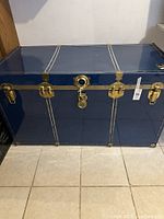 Front view of large blue metal trunk with brass hardware and lock, showing overall condition and design.