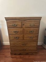 Front view of the wooden chest of drawers showing six drawers with metal handles and keyhole, medium brown wood grain finish.