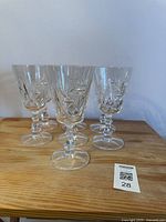 Set of six clear crystal wine glasses arranged on wooden surface, showing the detailed cut glass design and faceted stems.