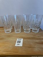 Front view of the set of 8 crystal water glasses on a wooden surface, 4 tapered and 4 cylindrical glasses, showing faceted crystal cut pattern.