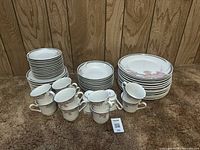 Complete view of the dishware set arranged on carpet, showing stacks of small, medium, and large plates near cups. Each piece features a pink floral pattern with silver trim.
