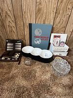 Group photo of all items showing game pieces in a wooden box, atlas, chip and dip ceramic tray, glass bowls, and card holder with playing cards on carpet