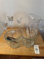 Photo showing two cut glass ice buckets, one containing metal tongs, three cut glass candle holders in a stand, and a cut glass pitcher on a wooden surface.
