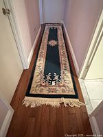 Hall runner rug laid out fully down a hallway on wooden floor, showing its full length and markings.