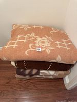 Stack of four heavy blankets folded corner to corner, showing the top blanket's floral and geometric cream pattern on an orange background