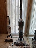 Two vacuum units side by side, one large Hoover upright vacuum and one smaller white unit, cords visible on floor