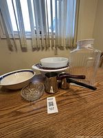 Photo shows 2 bowls, 2 Turkish coffee pots with handles, a large clear juice jug with lid, and 2 colanders stacked with a small round glass dish in front.
