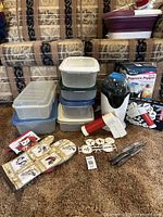 Full view of the popcorn maker, storage bins, cookie press with disks, oven mitt, pot holder, and tongs on carpeted floor in front of couches.