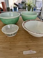 Four vintage bowls on a wooden surface with plants in the background, showing size and color differences between bowls.