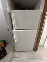 Full view of white top freezer refrigerator showing front with two doors and handles, positioned in a corner near a doorway and window.