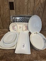 Photo showing various serving dishes arranged including rectangular, oval, and scalloped dishes with plain and floral patterns and a large metal embossed tray