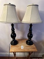 Front view of two black candle-style lamps with beige fabric shades placed on a small wooden table.