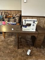 Sewing machine on a wooden table with power cord and drawers below