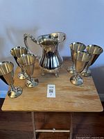 Full view of the vintage silver plated pitcher and six goblets on a wooden table with light background.