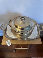 Full view of silver plated serving dish with lid resting on rectangular tray with handles.