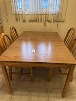 Full view of wooden dining table with four chairs, natural wood finish, sitting on tiled floor.