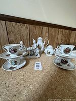 Front view of the porcelain tea set showing teapot, sugar bowl, three teacups on saucers, and two figurines