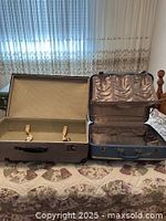 Two vintage hard case suitcases opened to show interiors and exteriors, laid on a floral bedspread.