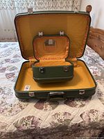 Open large green hard shell suitcase with matching vanity case inside, showing yellow interior and small mirror.
