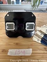 Front view of black vintage View-Master with two eye lenses, placed on wooden surface with photo reel packets beside it.