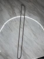 Full view of the 18-inch silver rope chain necklace laid flat on a marble surface, showing the length and twisted rope design.